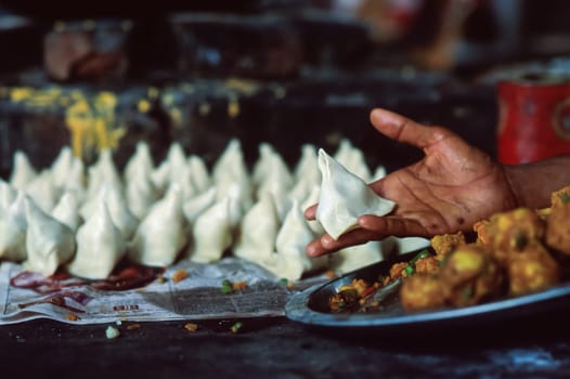 Horizontal image of a male hand holding a samosa ready for cooking and in the blurred background other numerous pieces resting on sheets of newspaper, traditional street food, North India