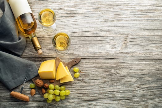 Bottle of white wine with snack food on old board. Glass of wine and cork. Wine bottle mockup. Top view