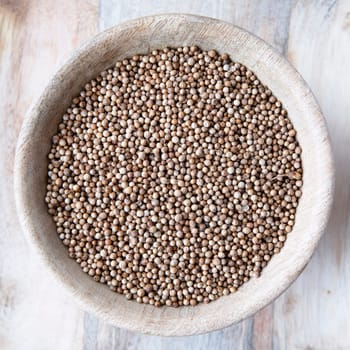 Flat lay wooden bowl of whole coriander seeds