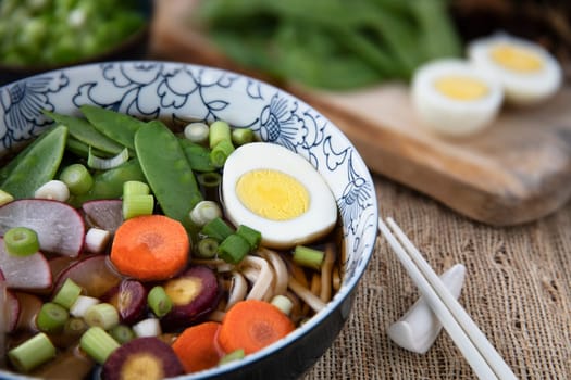 Colorful fresh bowl of udon noodle and vegetable soup with chopsticks.