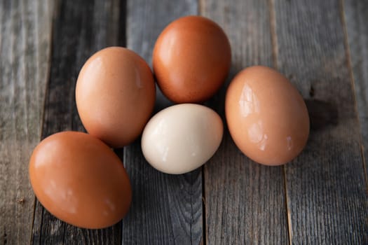 Close-up of brown eggs and one small lighter egg on wooden table.