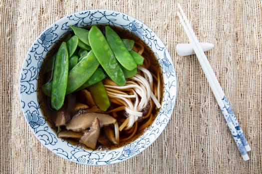 Filling bowl with udon noodle soup series image five: bowl withnoodles, shiitake mushrooms, snow peas, and broth.