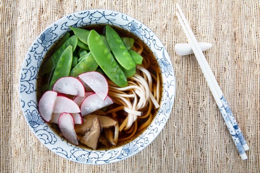 Filling bowl with udon noodle soup series image six: bowl with noodles, shiitake mushrooms, snow peas, broth, and radishes.