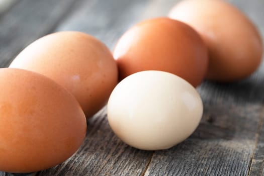 Close-up of brown eggs and one small lighter egg on wooden table.