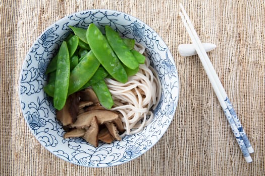 Filling bowl with udon noodle soup series image four: bowl withnoodles, shiitake mushrooms, and snow peas.