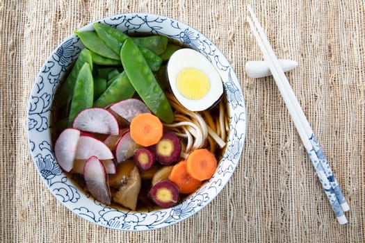 Filling bowl with udon noodle soup series image eight: bowl with noodles, shiitake mushrooms, snow peas, broth, radishes, carrots, and egg.