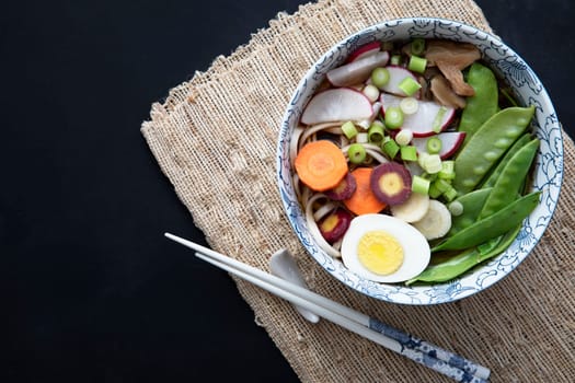 Flat lay of vegetable and egg udon noodle soup with chopsticks.