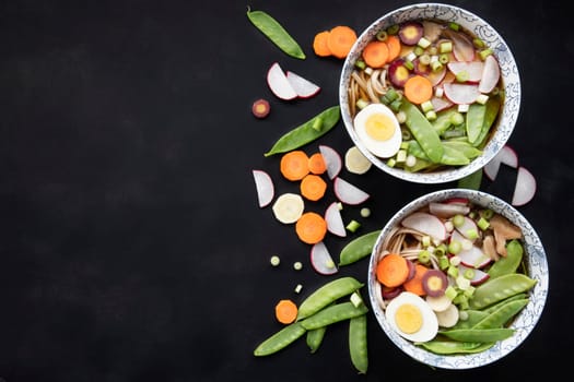 Two bowls of udon nooodle soup with fresh vegetables and hard boilled egg: flat lay with copy space.