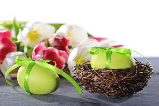green Easter egg with bow in the Easter nest with tulips in the background