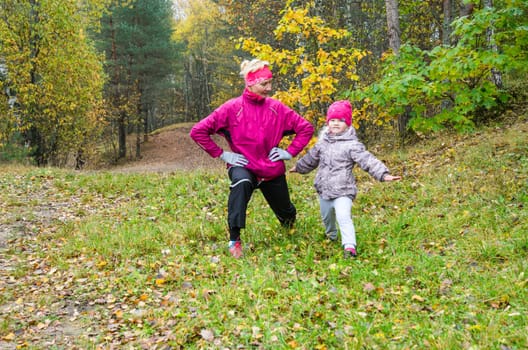 Woman with girl doing aerobics in the autumn park