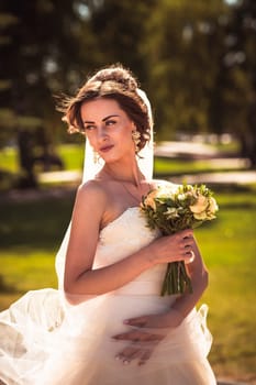 The beautiful brunette bride on a walk in park.