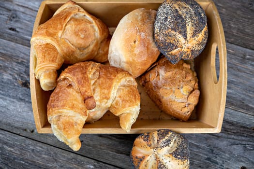 different fresh rolls and croissants in wooden basket in top view
