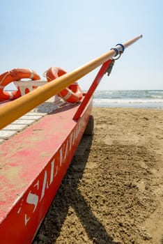 Red rescue boats on an italian beach, a blue sky in background. On the boat there is words meaning safeguard in italian