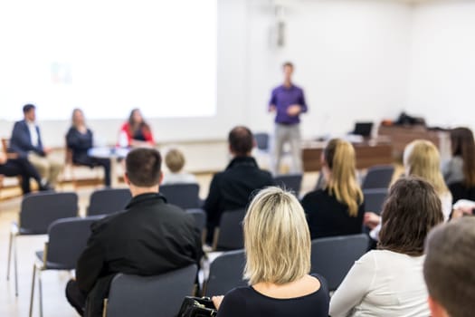 Business and entrepreneurship symposium. Speaker giving a talk at business meeting. Audience in the conference hall. Rear view of unrecognized participant in audience.
