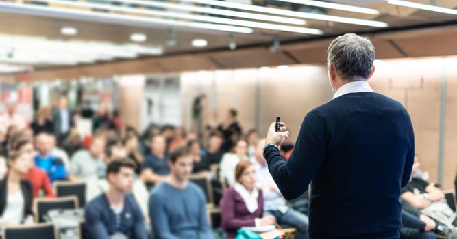 Expert giving a talk on business conference workshop. Unrecognizable people in audience at the conference hall. Business and entrepreneurship event.