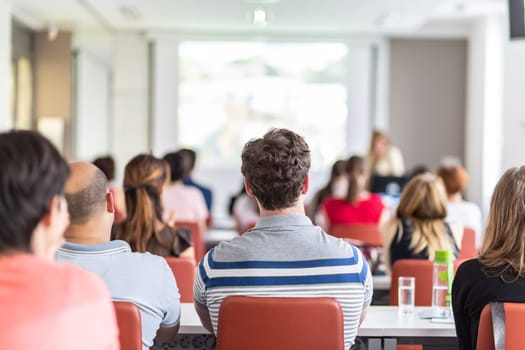 Female speaker giving presentation in lecture hall at university workshop. Audience in conference hall. Rear view of unrecognized participant in audience. Scientific conference event.