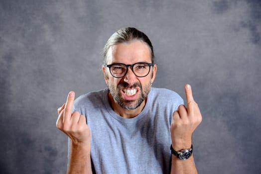 young man in front of gray background showing middle finger