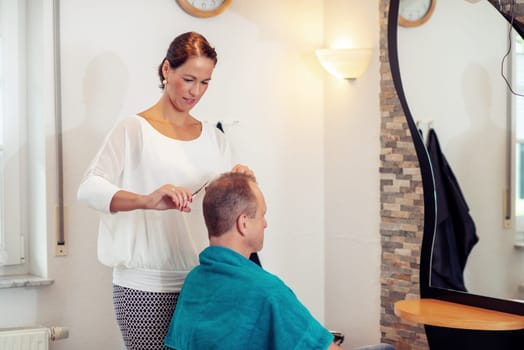 female hairdresser cutting hair of man in her shop