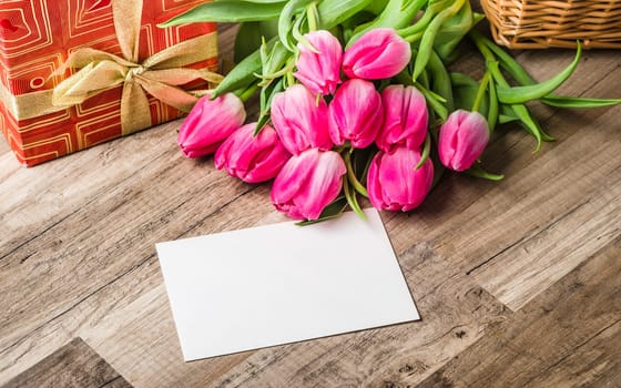 Beautiful bouquet from pink tulips and a gift on a table