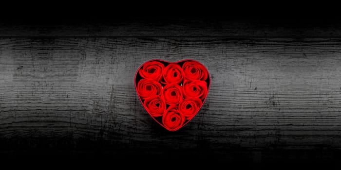 Red roses in a heart-shaped box on black wooden background