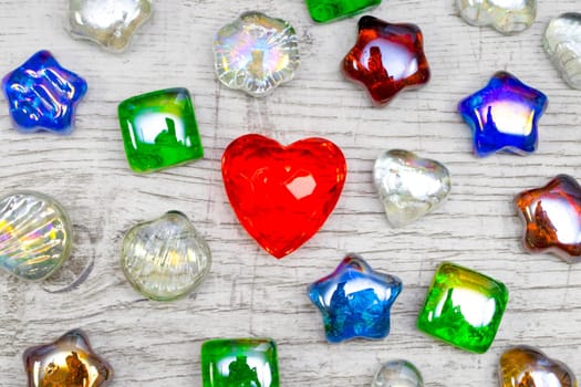 Shiny red ruby heart shape and glass stones on wooden background