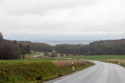 Curving road between fields and trees in Germany Langgöns in Winter with Rain