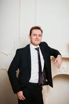 Portrait groom man in black suit on light background.
