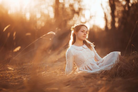 girl is sitting in the field on the sunset background.