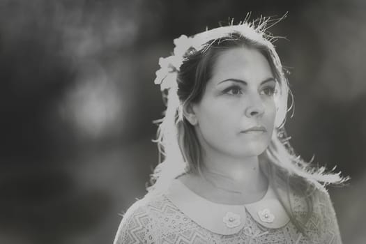 Blackwhite photo portrait of a girl in a field on a sunset background.