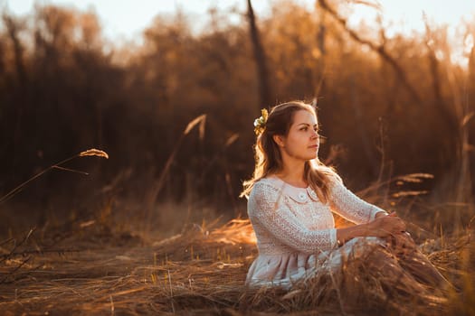 girl is sitting in the field on the sunset background.