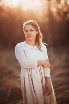 Beautiful girl standing in a field on a sunset background.