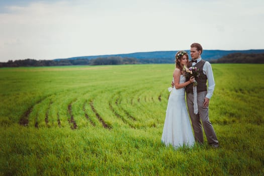 bride and groom stand on the background of the field.