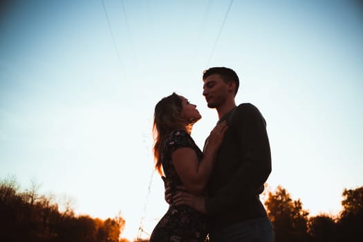 Silhouettes of a guy and girl in a field on a sunset background.