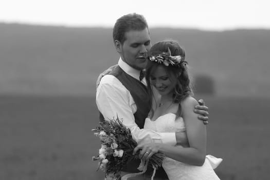 black white photo portrait bride and groom stand on the background of the field.