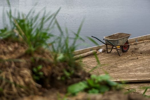 Wheelbarrow for construction in site building area at the river. Construction wheelbarrow and shovel in the sand by the river Daugava, Latvia.