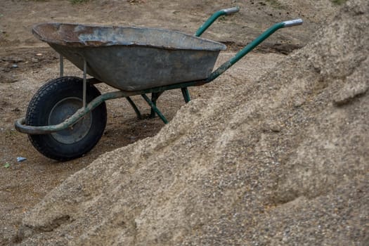 Construction wheelbarrow in the sand by the river Daugava. Wheelbarrow at the gravel pile, Latvia. Wheelbarrow for construction in site building area.