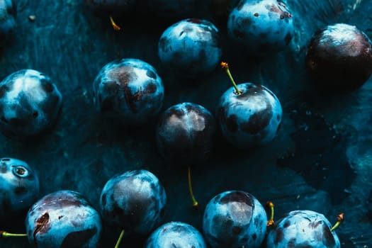 many fresh plums on blue background close up