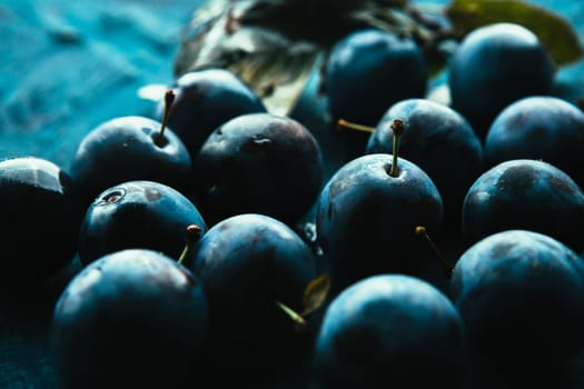 many fresh plums on blue background close up.
