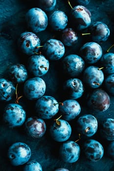 many fresh plums on blue background close up