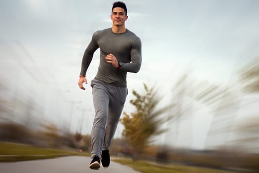 The handsome sporty man is jogging outdoors at the street.