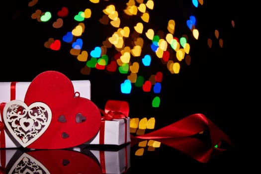 Gift boxes and decorative hearts on a black background with heart-shaped bokeh . Valentine's Day card with copy space. Design element for romantic greeting card, wedding invitation