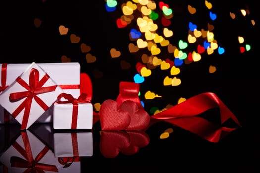 Gift boxes and red satin hearts on a black background with heart-shaped bokeh . Valentine's Day card with copy space. Design element for romantic greeting card, wedding invitation