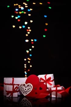 Gift boxes and red hearts on a black background with heart-shaped bokeh . Valentine's Day card with copy space. Design element for romantic greeting card, wedding invitation