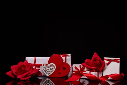 Gift boxes and red roses and decorative heart on black background. Valentine's Day card with copy space. Design element for romantic greeting card, wedding invitation