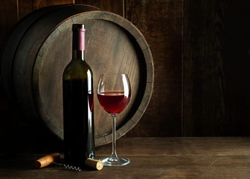 Bottle of red wine with glass on wooden and barrel background. Glass of wine and cork.