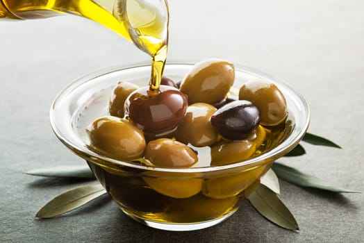 Organic olive oil. Bottle of Extra virgin oil pouring in to glass bowl with olives