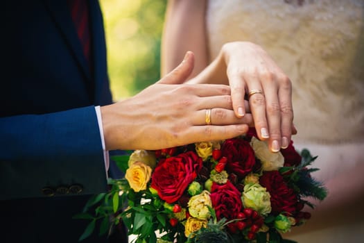 hands of the bride and groom on a bouquet.