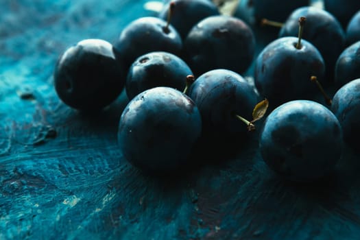 many fresh plums on blue background close up.