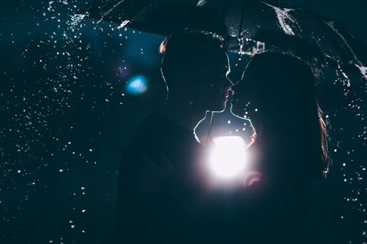 young couple standing under a dark umbrella.