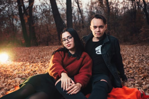 young man and young woman are sitting on a plaid in an autumn forest.